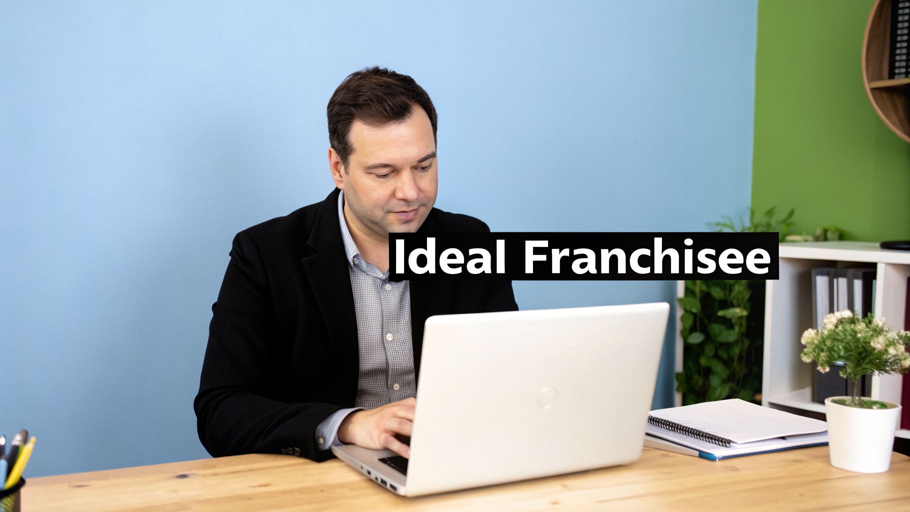 Businessman focusing on his laptop with 'Ideal Franchisee' text over a split blue and green wall.